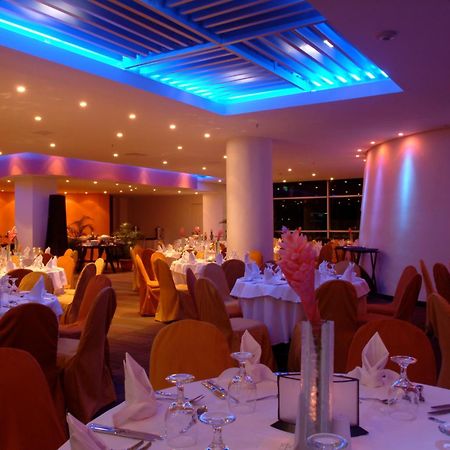Decapolis Hotel ปานามาซิตี้ สิ่งอำนวยความสะดวก รูปภาพ The image shows an elegant restaurant interior. The dining area features round tables covered with white tablecloths, and each table is set with glassware and napkins. The chairs are draped in orange fabric, contributing to a warm and inviting atmosp