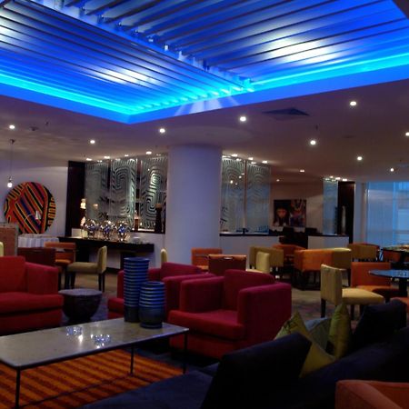 Decapolis Hotel ปานามาซิตี้ ร้านอาหาร รูปภาพ The photo shows a modern lounge or lobby area with various seating arrangements. The furniture includes colorful chairs and sofas, predominantly in shades of red, pink, and yellow, arranged around glass-topped tables. The ceiling features a blue illu