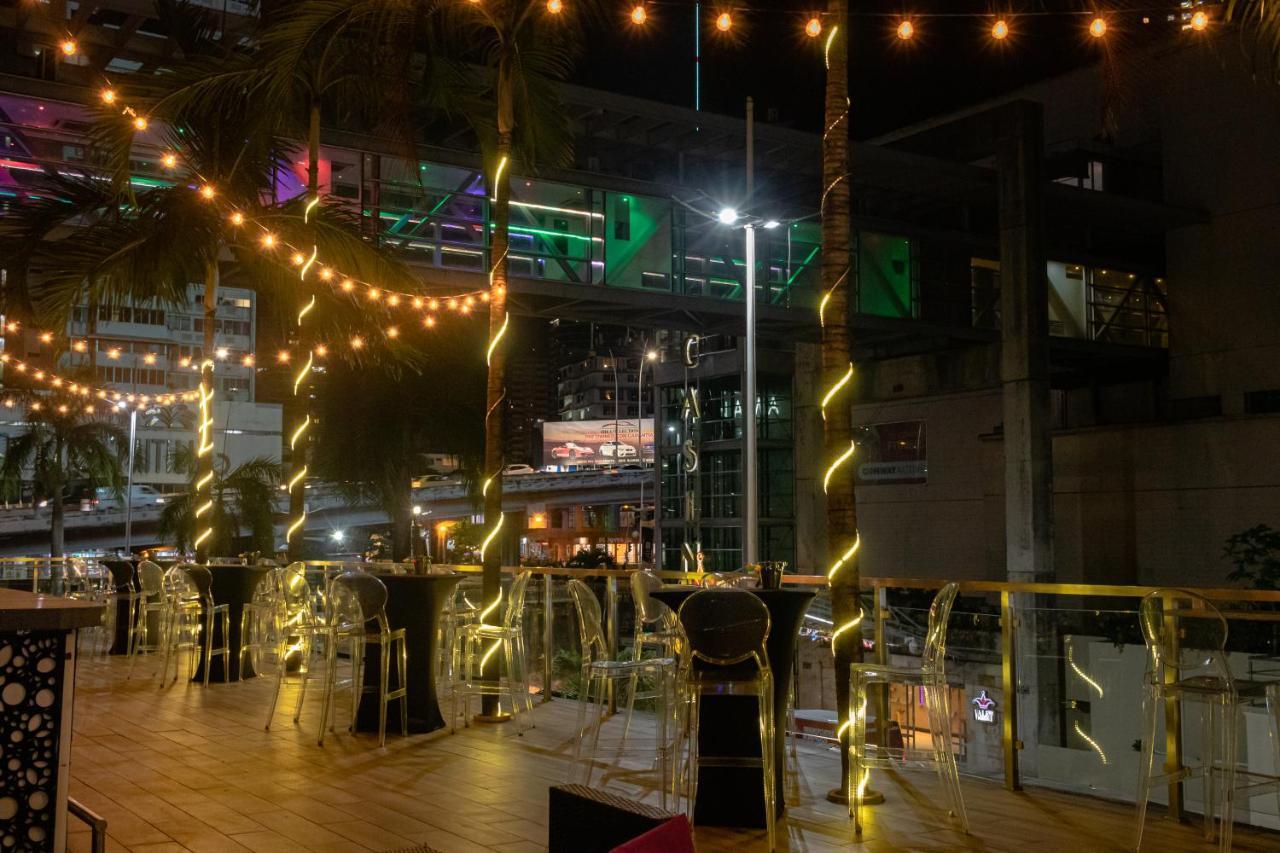 Decapolis Hotel ปานามาซิตี้ ภายนอก รูปภาพ The photo shows an outdoor seating area, likely at a restaurant or bar. It features several tall tables with transparent chairs around them. The space is illuminated with string lights that create a warm and inviting atmosphere. In the background, th