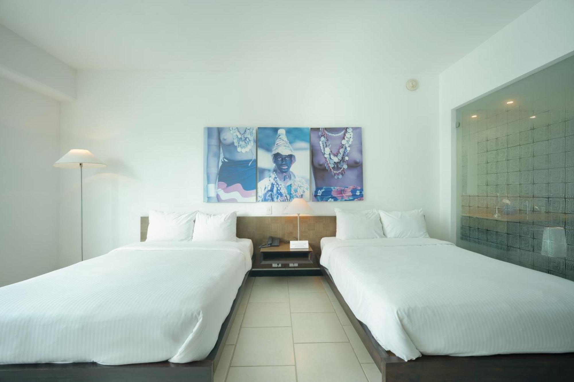 Decapolis Hotel ปานามาซิตี้ ภายนอก รูปภาพ The photo shows a modern hotel room featuring two double beds with white bedding. The walls are painted a light color, contributing to a clean and minimalist aesthetic. Above the beds, there is a large piece of artwork that displays a colorful design