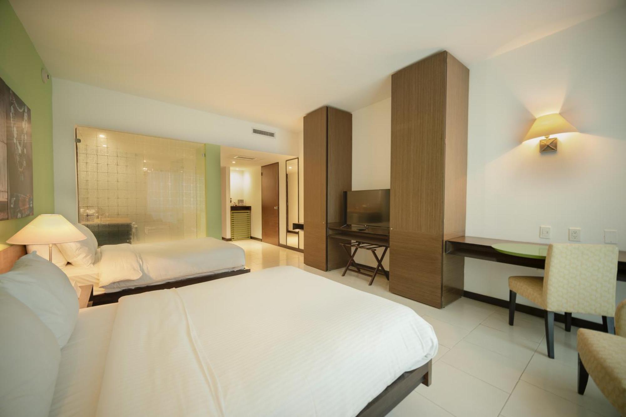 Decapolis Hotel ปานามาซิตี้ ภายนอก รูปภาพ The photo shows a modern hotel room featuring two beds with white bedding. There is a large window allowing for natural light, and one wall is occupied by built-in cabinets and a flat-screen TV. A small desk with a chair is positioned near the TV, an