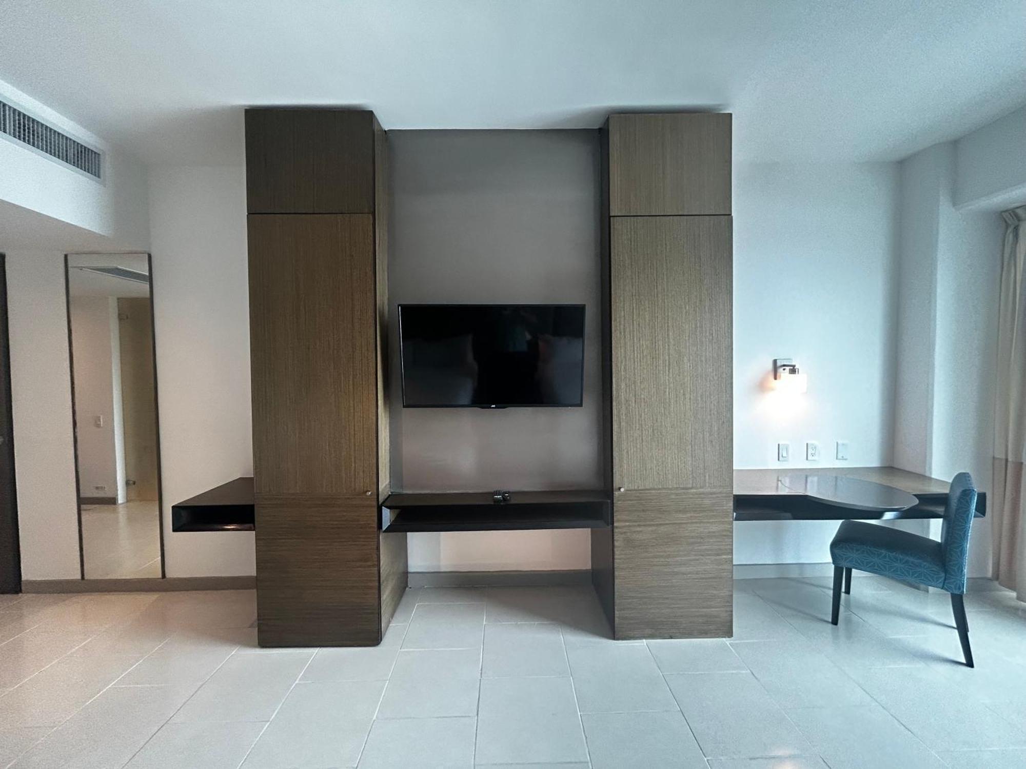 Decapolis Hotel ปานามาซิตี้ ภายนอก รูปภาพ The photo shows a modern interior space, likely a hotel or apartment room. Central to the image is a mounted flat-screen television on a wall, flanked by tall, narrow cabinets or panels made of a wood-like material. Below the TV, there is a long, dar